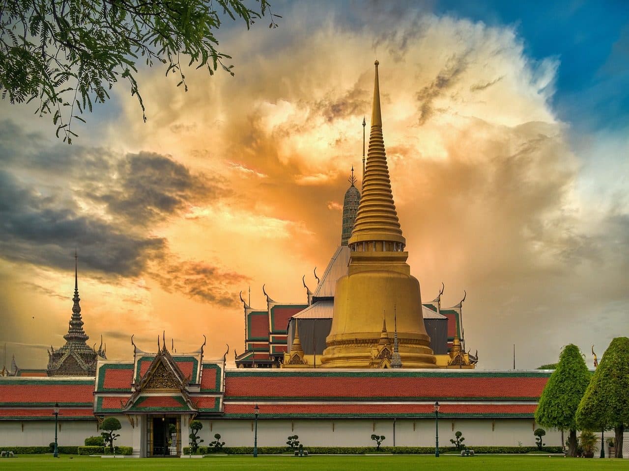 A golden chedi and temple roofs under a dramatic sky in Bangkok