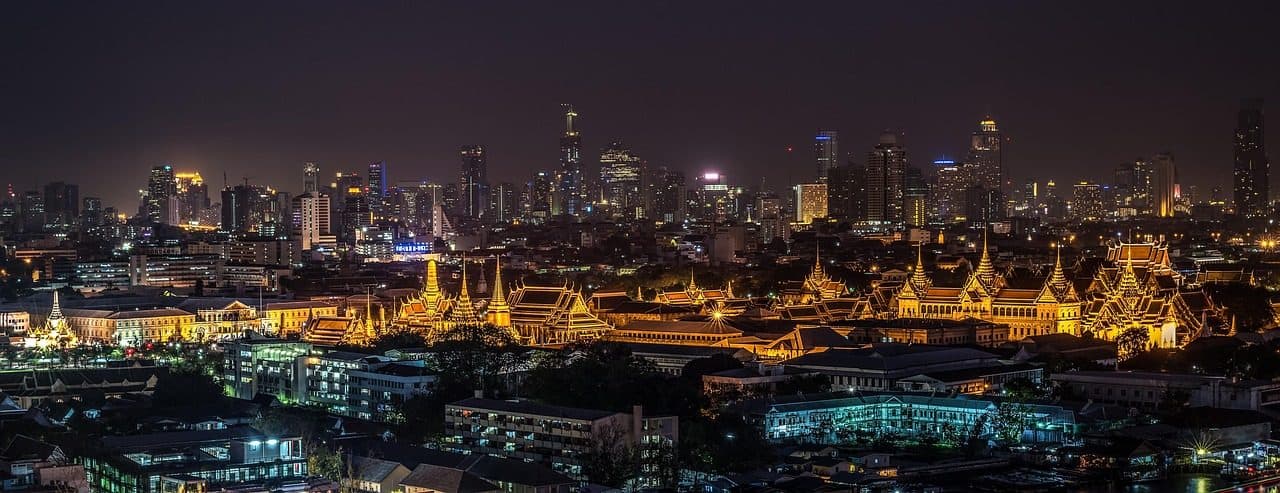 The Grand Palace lit up at night, with Bangkok's skyline behind it