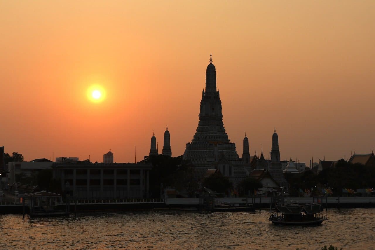 Wat Arun silhouetted against an orange sunset sky over the river